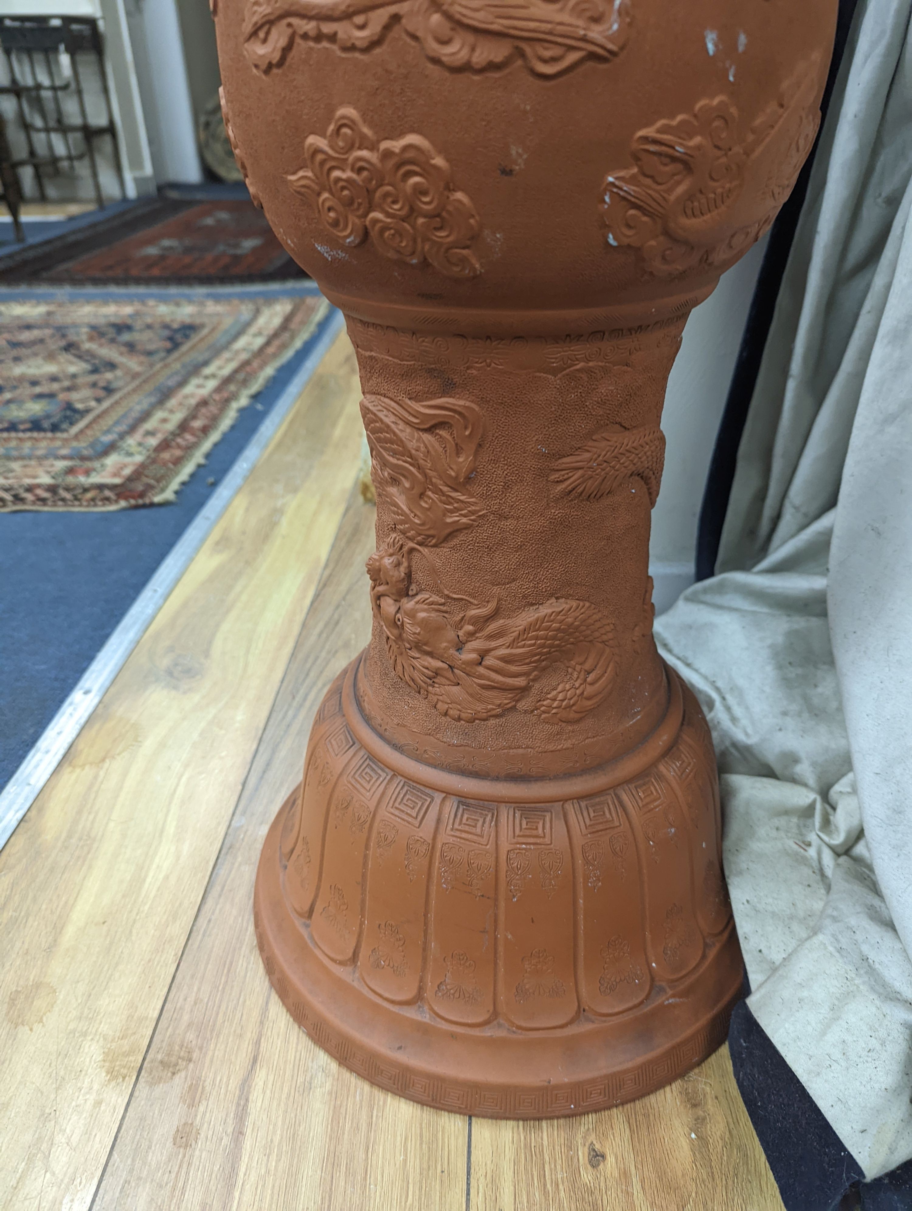 A Chinese earthenware jardiniere on stand moulded with dragons. Height 99 cms.